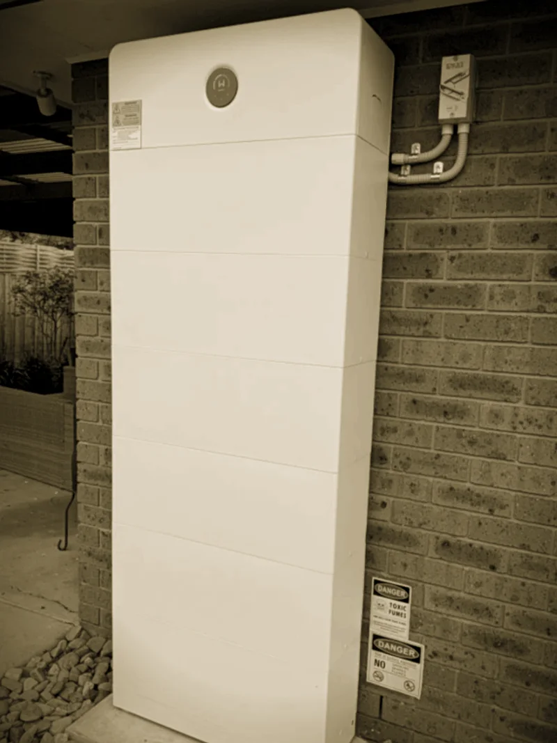 A tall white battery stack installed by Primero beside a carport