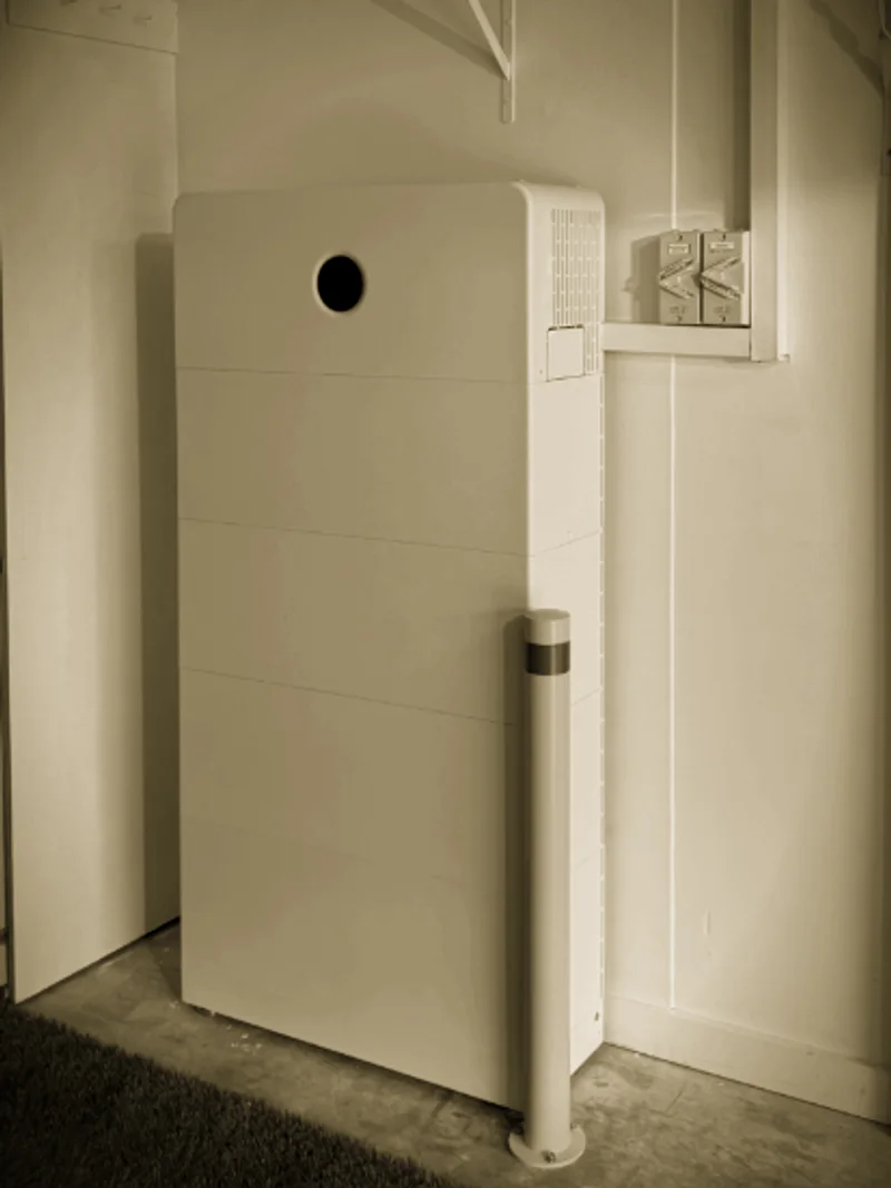 A white battery stack installed by Primero in a garage, behind a bollard