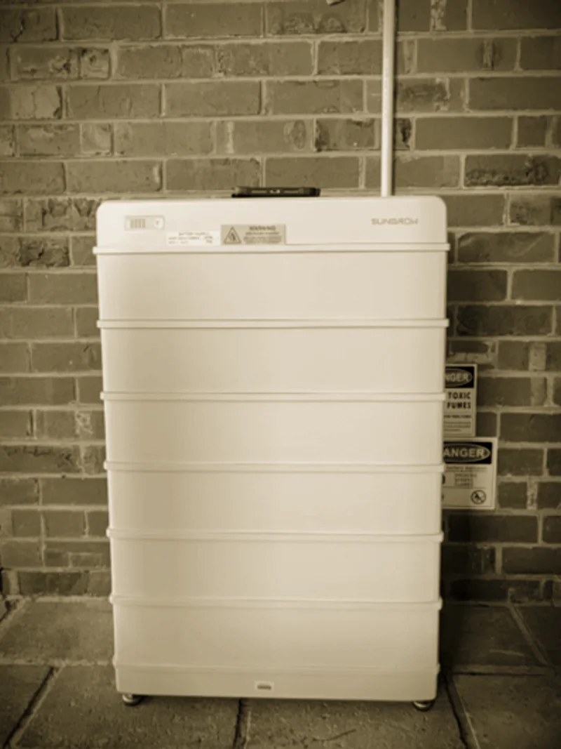A Sungrow battery stack installed by Primero against a red brick wall